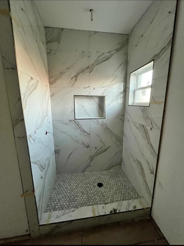 Light marble shower with a window and hexagonal floor tile.