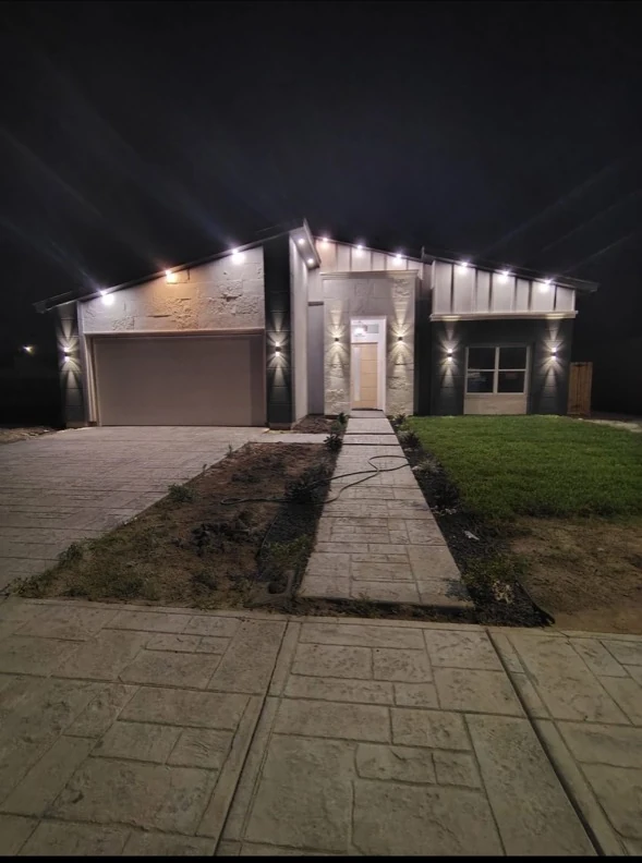 Residential home illuminated at night beside a concrete walkway.