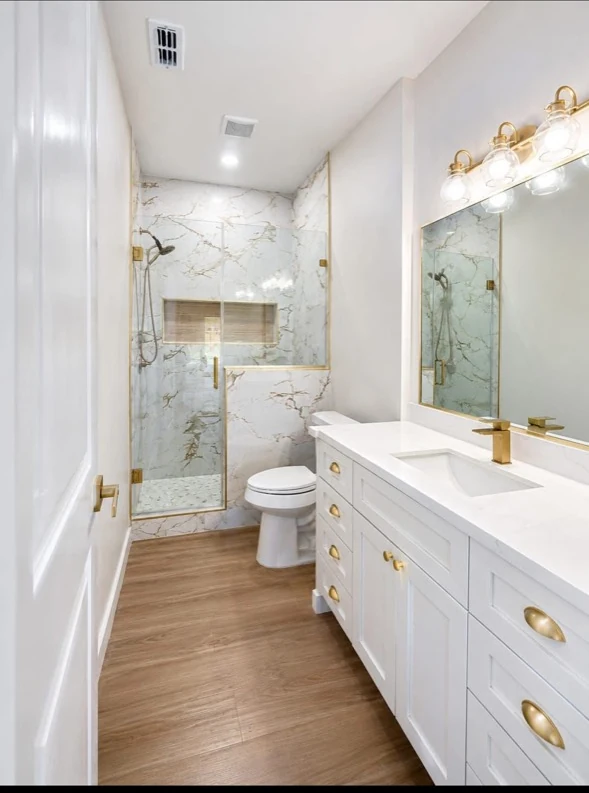 Bathroom with glass shower, white vanity, and gold-tone hardware.